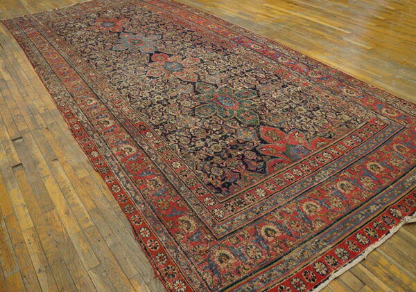 Ornate traditional low-pile rug featuring a red border and dark blue field on worn wooden planks.