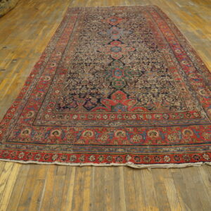 Navy and red traditional area rug with a detailed medallion pattern lies on worn wooden flooring.