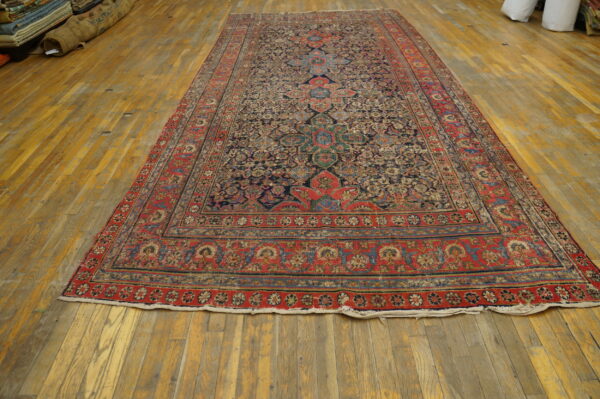 Navy and red traditional area rug with a detailed medallion pattern lies on worn wooden flooring.