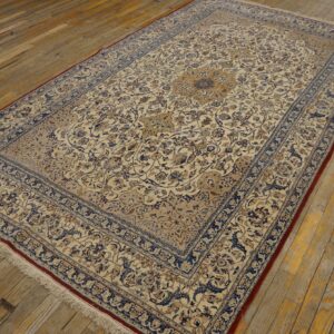 Traditional cream rug with intricate blue and gold floral patterns rests on aged wooden floorboards.