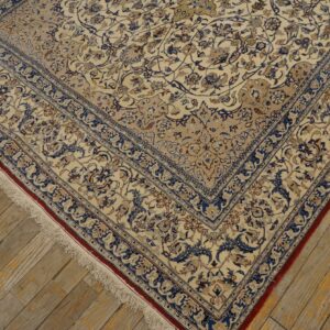 Ornate cream rug with blue floral design and fringe edges resting on worn wooden floorboards.
