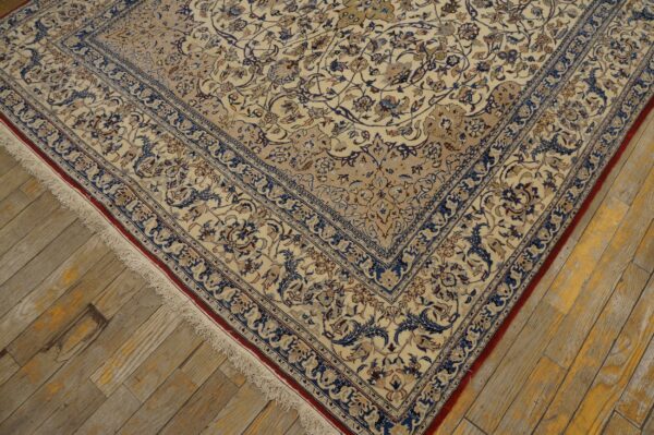 Ornate cream rug with blue floral design and fringe edges resting on worn wooden floorboards.