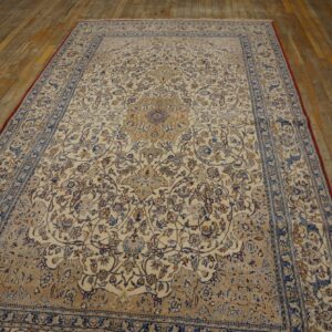 Traditional cream rug with a blue and tan repeating floral design laid on worn wood plank flooring.