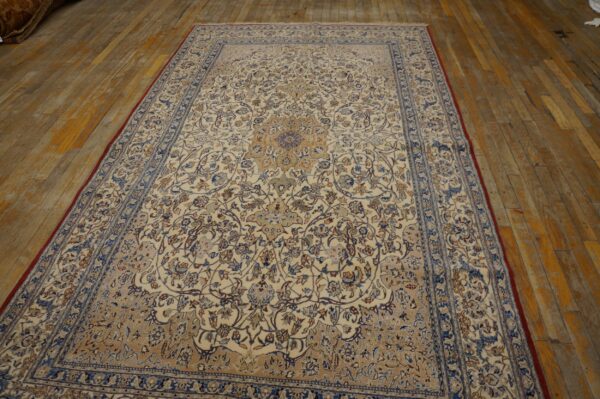 Traditional cream rug with a blue and tan repeating floral design laid on worn wood plank flooring.