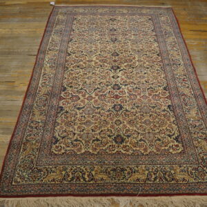 Low-pile beige and multi-colored traditional rug with dense floral patterns rests on distressed wood flooring.
