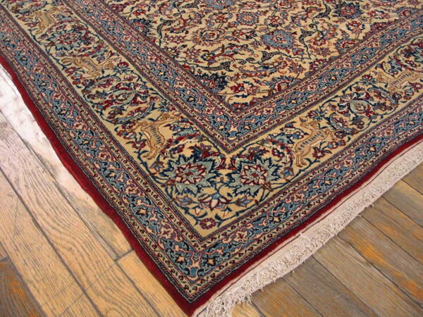 Beige rug corner with dense blue, red, and tan traditional pattern and a dark red edge on wood planks.