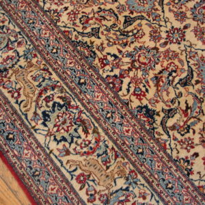 Detailed ivory rug showing red and blue floral patterns, a striped border, and a tan feline figure on wood flooring.