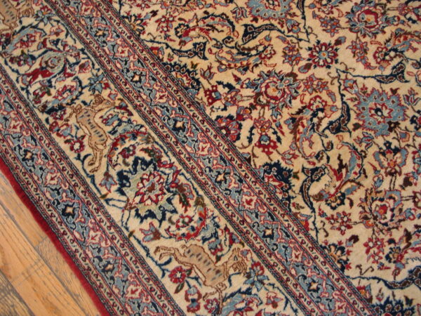 Detailed ivory rug showing red and blue floral patterns, a striped border, and a tan feline figure on wood flooring.