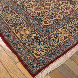 Cream traditional rug with red and blue floral borders rests on light weathered hardwood flooring.