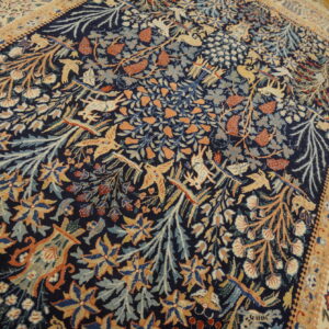 Dark blue rug featuring a dense pattern of orange, gold, and light blue stylized birds, deer, and foliage.
