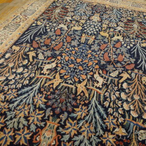Navy rug with a dense tan, rust, and blue pattern of animals and foliage resting on wood floorboards.