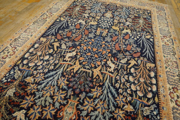 Navy rug with a dense tan, rust, and blue pattern of animals and foliage resting on wood floorboards.