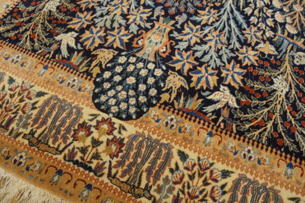 Intricate low-pile rug with navy blue field, tan border, and detailed peacock and bird motifs.