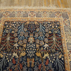 Low pile rug in navy blue and gold with complex botanical and creature patterns on rustic wood planking.