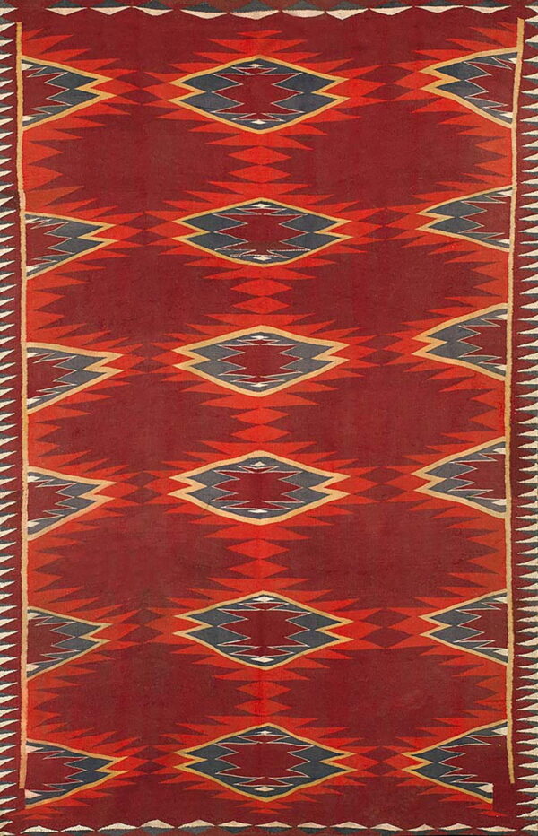 Vertical geometric rug with serrated red diamonds and dark blue centers on a deep red background.