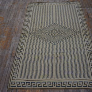 Cream flatweave rug featuring a blue zigzag pattern, central medallion, and Greek key border on distressed wood.