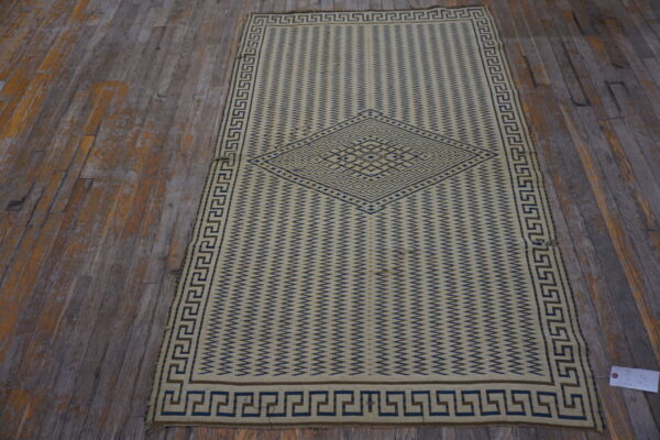 Cream flatweave rug featuring a blue zigzag pattern, central medallion, and greek key border on distressed wood.