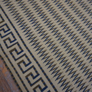 Flat-weave rug featuring a beige field, blue and brown zigzag pattern, and geometric border on wood planks.