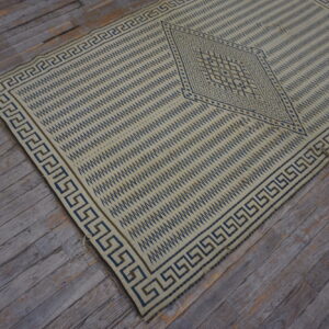 Cream flatweave rug featuring dark blue geometric patterns and a Greek key border on distressed wood flooring.