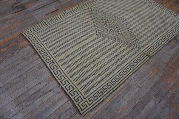 Cream flatweave rug featuring dark blue geometric patterns and a greek key border on distressed wood flooring.