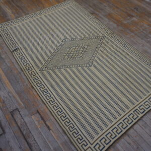 Cream and blue geometric rug with a Greek key border lies on rustic, grey wood planks.