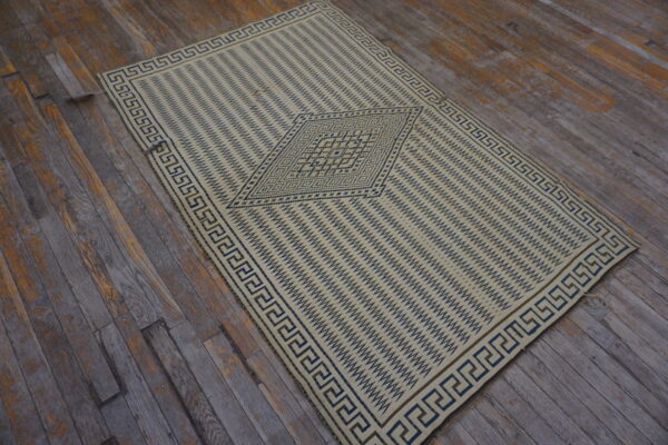 Cream and blue geometric rug with a greek key border lies on rustic, grey wood planks.