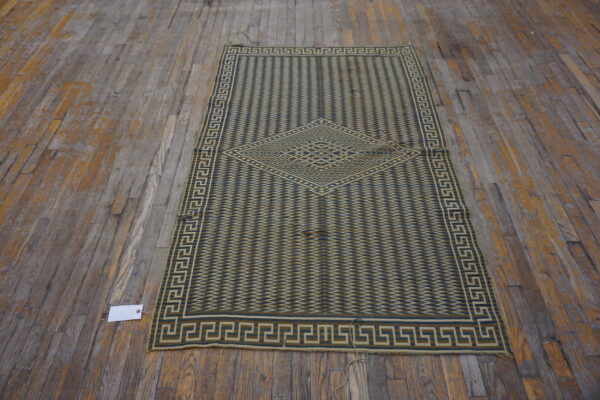 A low-pile green and tan runner with a geometric medallion rests on distressed wide plank flooring.