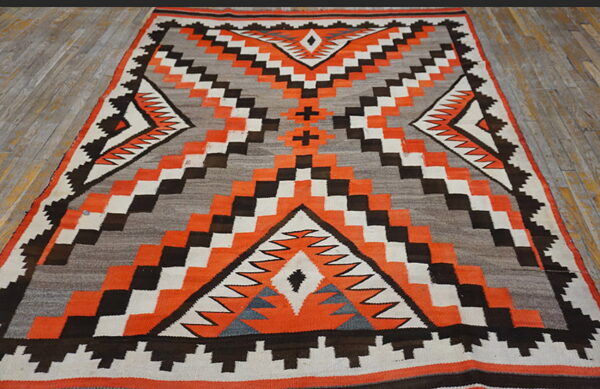 Geometric flatweave rug featuring orange, black, white, and gray patterns, displayed on a plank wood floor.