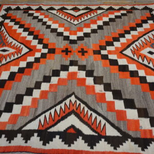 Geometric flat-weave rug in orange, gray, black, and white on distressed wood flooring.