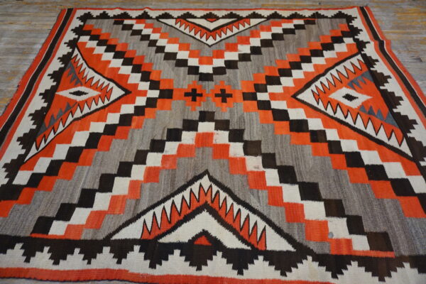 Geometric flat-weave rug in orange, gray, black, and white on distressed wood flooring.