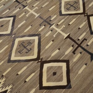 Flatweave rug in browns and cream with geometric diamonds, diagonal stripes, and stylized cross symbols.