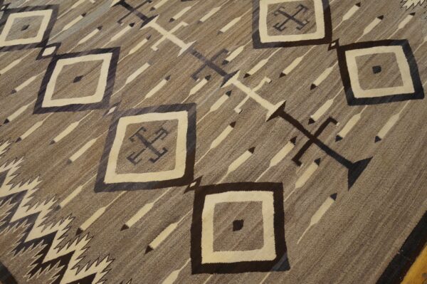 Flatweave rug in browns and cream with geometric diamonds, diagonal stripes, and stylized cross symbols.