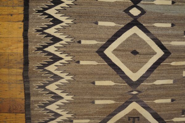 Brown, cream, and dark geometric flatweave rug featuring diamond and zigzag motifs on a wood floor.