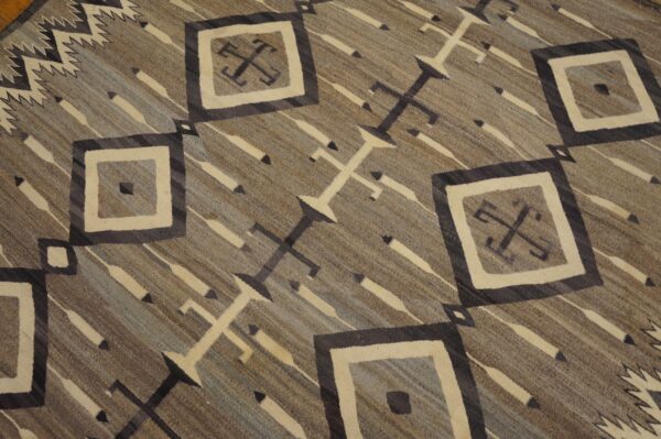 Low-pile geometric rug featuring diamonds, crosses, and diagonal stripes in gray, brown, and cream tones.