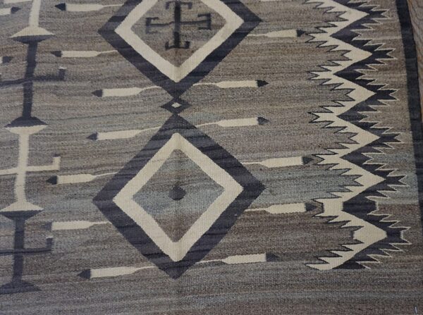 Gray and taupe flat-weave rug with geometric diamonds, cross motifs, and zigzag borders in charcoal and cream.
