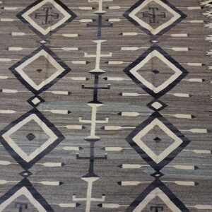 Muted gray and taupe flatweave rug displaying geometric patterns of cream diamonds and dark central crosses.