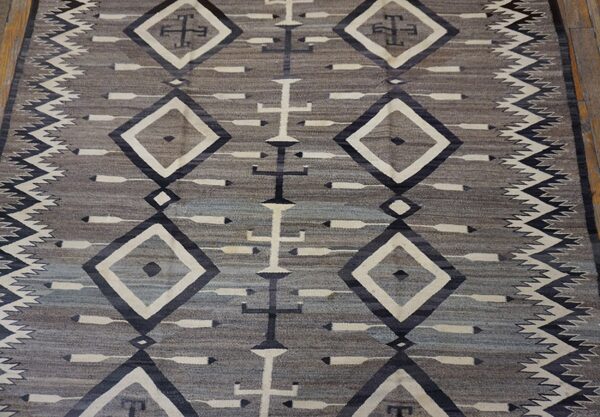 Muted gray and taupe flatweave rug displaying geometric patterns of cream diamonds and dark central crosses.