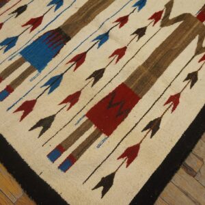 Cream and brown flatweave rug with stylized human figures, red and blue arrows, and a black border on wood planks.