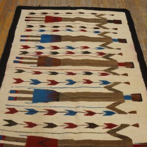 Flat-weave cream rug with brown, red, and blue geometric figures and arrows on rustic wood flooring.