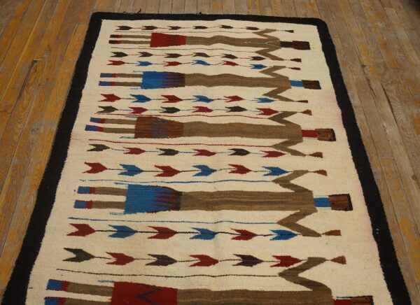 Flat-weave cream rug with brown, red, and blue geometric figures and arrows on rustic wood flooring.