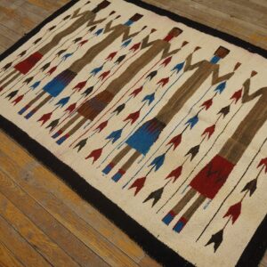 A cream flat-woven rug featuring brown abstract figures and red and blue arrows lies on worn wood flooring.