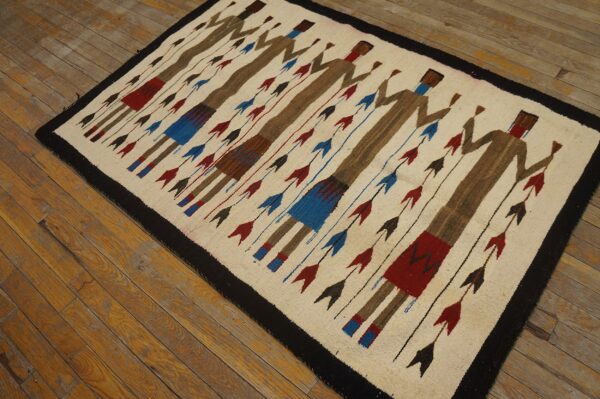 A cream flat-woven rug featuring brown abstract figures and red and blue arrows lies on worn wood flooring.