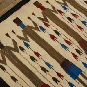 Cream rug with brown stylized figures and rows of red and blue arrow motifs on plank flooring.