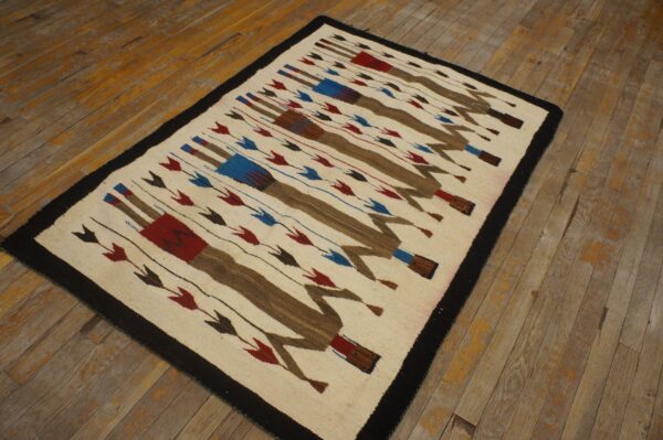 Low-pile cream rug featuring brown, red, and blue repeating figures on worn wooden flooring.