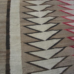 A flatweave rug with brown, grey, and red geometric zigzag patterns rests on wood floorboards.