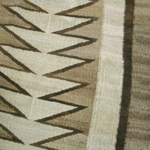 Close-up of a flatweave rug featuring cream, tan, and dark brown zigzag patterns on wood flooring.