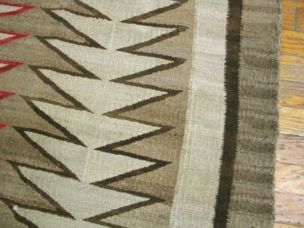 Close-up of a flatweave rug featuring cream, tan, and dark brown zigzag patterns on wood flooring.
