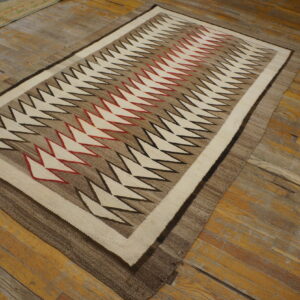 Cream, brown, red, and black zig-zag patterned flatweave rug resting on distressed hardwood flooring.
