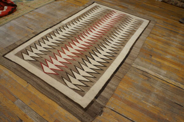 Cream, brown, red, and black zig-zag patterned flatweave rug resting on distressed hardwood flooring.