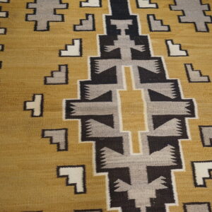 Geometric flatweave rug in gold, black, gray, and cream sits on light wood flooring.